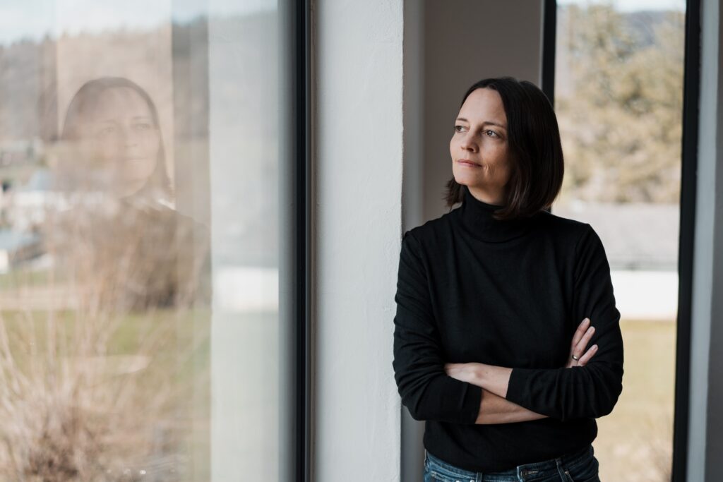 a serious woman in black looks out a window